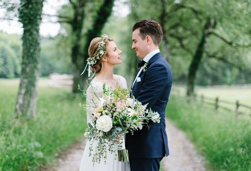 Brautpaar steht auf Feldweg mit großem Blumenstrauss und betrachtet sich